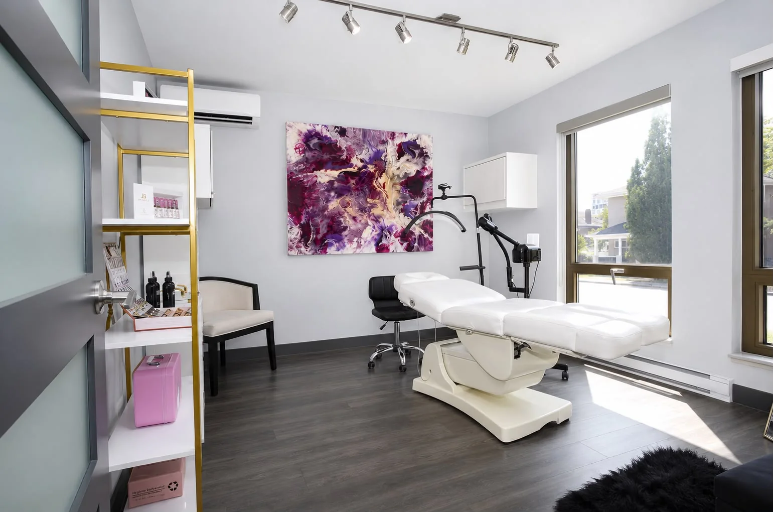 Facial treatment room with treatment bed, magnifying lamp and a large artwork